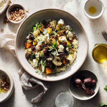 Modern Midden-Oosters gerecht geserveerd in een grote schaal op een koelgetinte, lichtgekleurde stenen ondergrond. Het hoofdgerecht is een kleurrijke een mezze-achtige schaal met geroosterde groenten, verse kruiden en gerooste