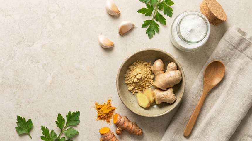 flat lay van verse gember in een schaaltje, met daarnaast vitamine c poeder, kurkuma, knoflook en peterselie